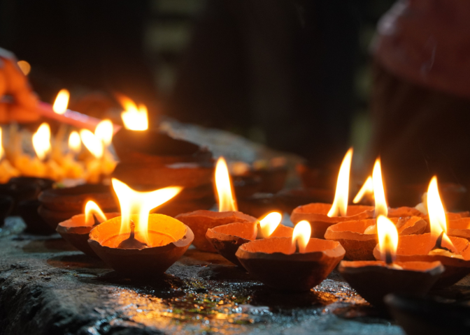 Flames flicker in a row of clay lamps, lined up on a stone surface in celebration of Diwali.