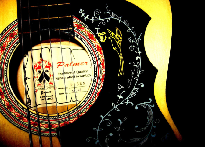 A Palmer folk guitar with an intricate vine and bird motif on the pick guard and a folk design around the sound hole.