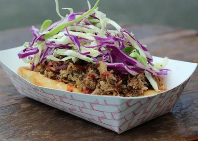An INDN taco sits in a paper boat, vegetables piled on top.
