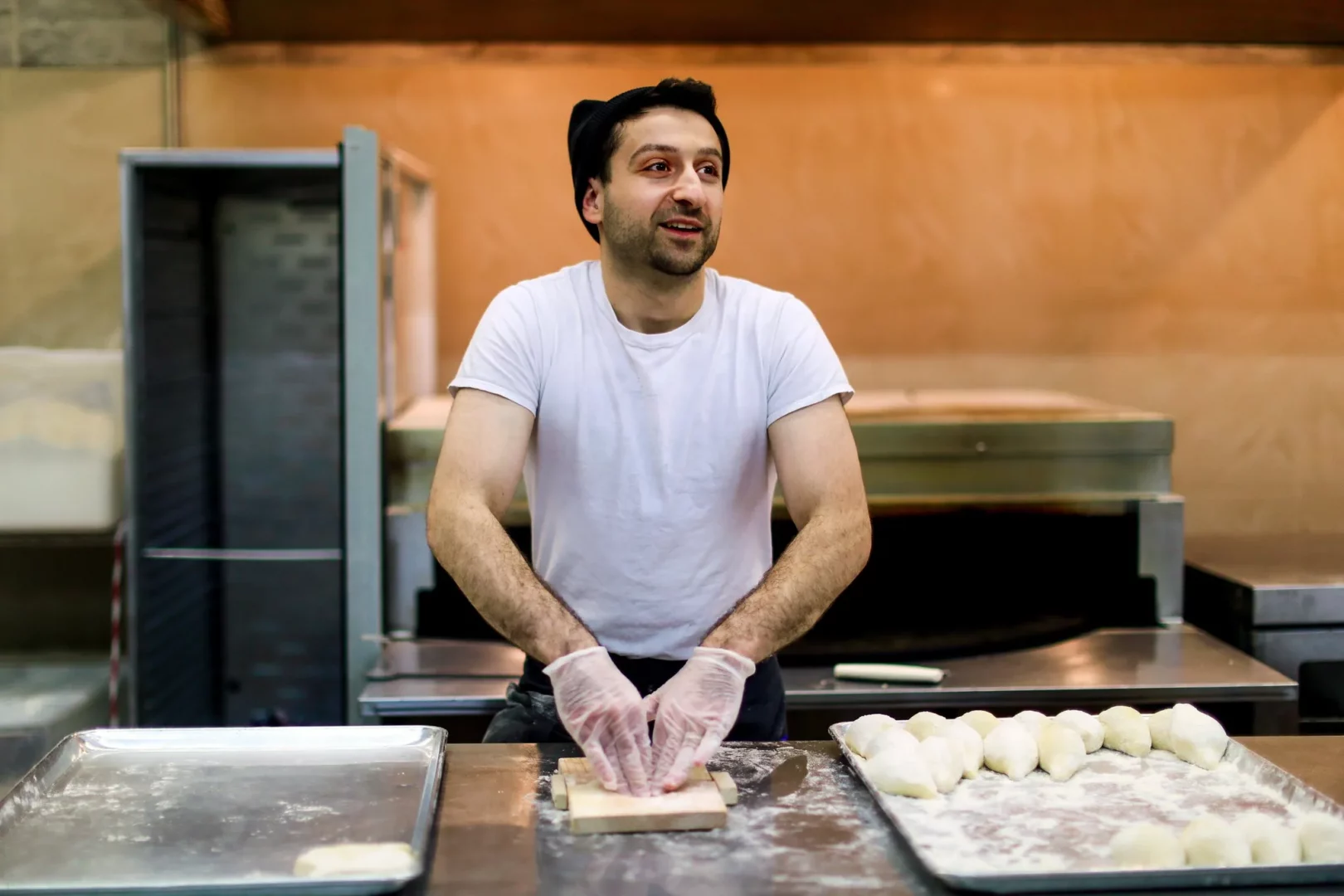 A man in a t-shirt kneads dough in a kitchen.