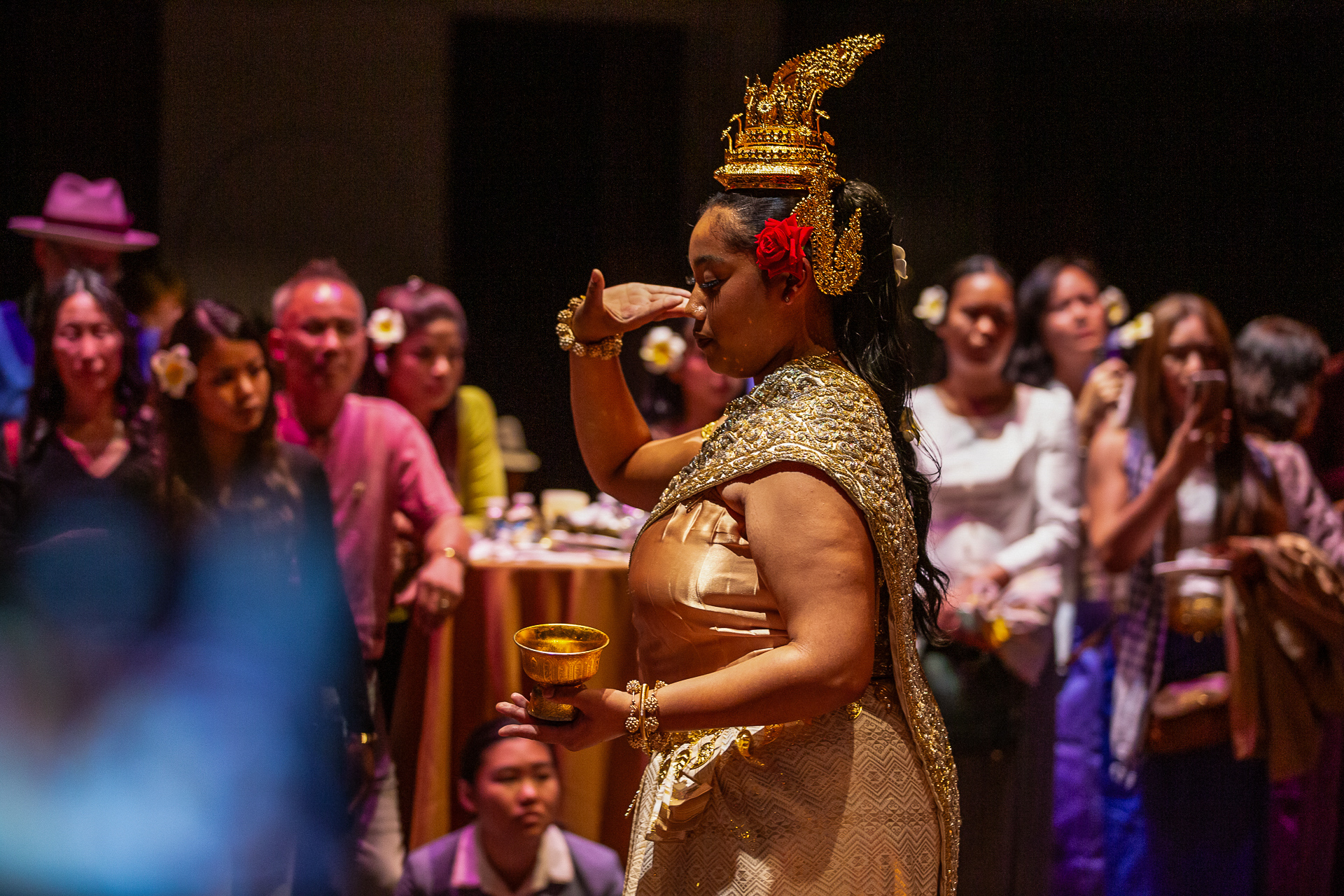 A woman in a gold dress and draped in gold adornments dances for a crowd.