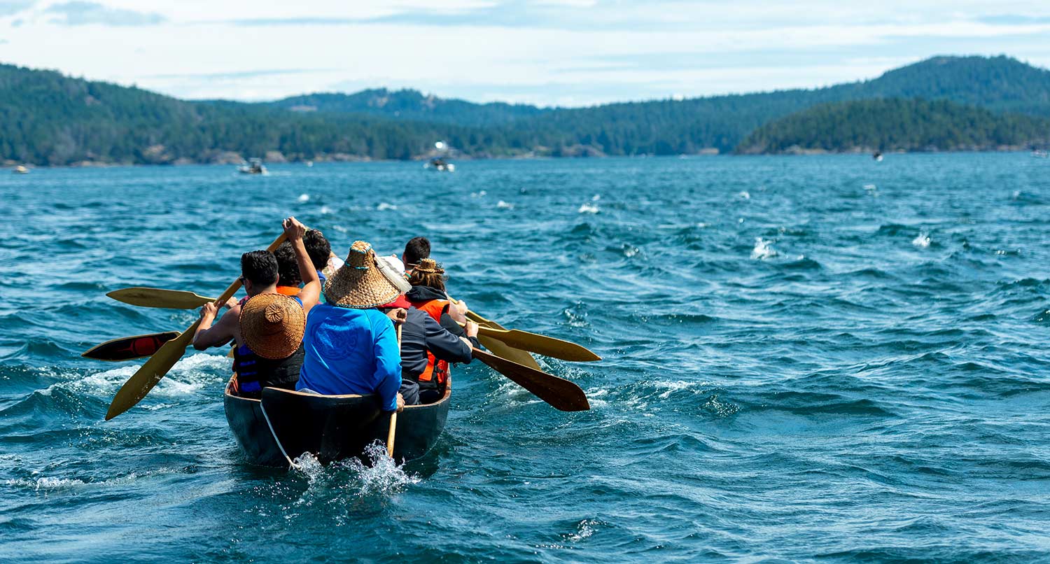 A group of people rowing in a canoe across a body of water.