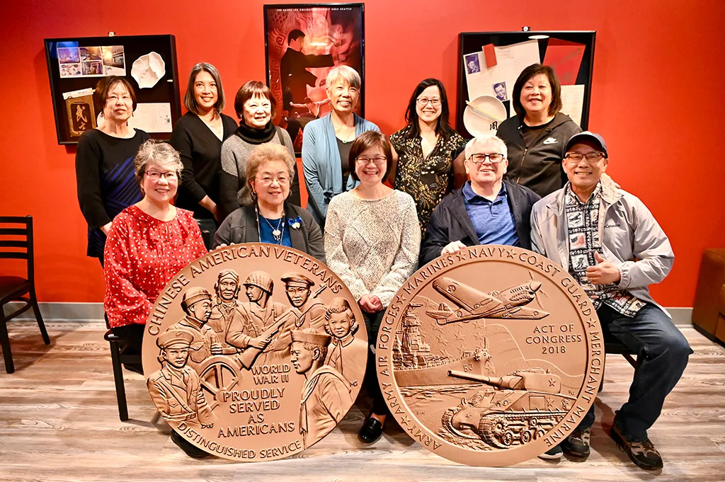 A group of Chinese Americans poses with giant medals depicting Chinese American veterans and their role in World War II.