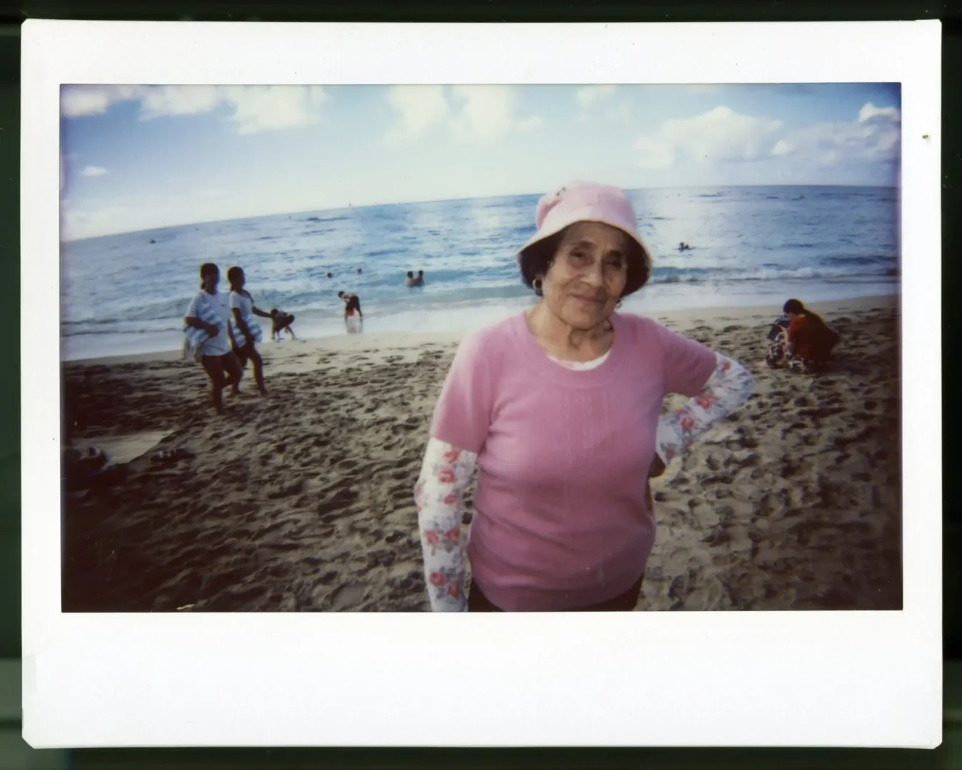 A woman in a matching hat and shirt stands on the beach smiling at the camera.