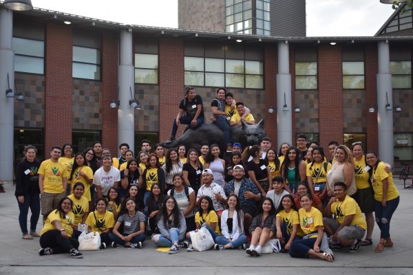 A group of students sit around a statue in front of a building.