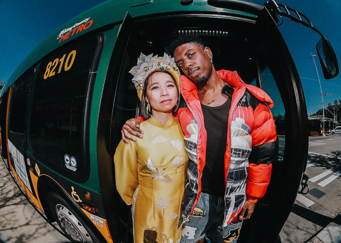 A black man and Asian woman pose for a photo in front of a King County bus