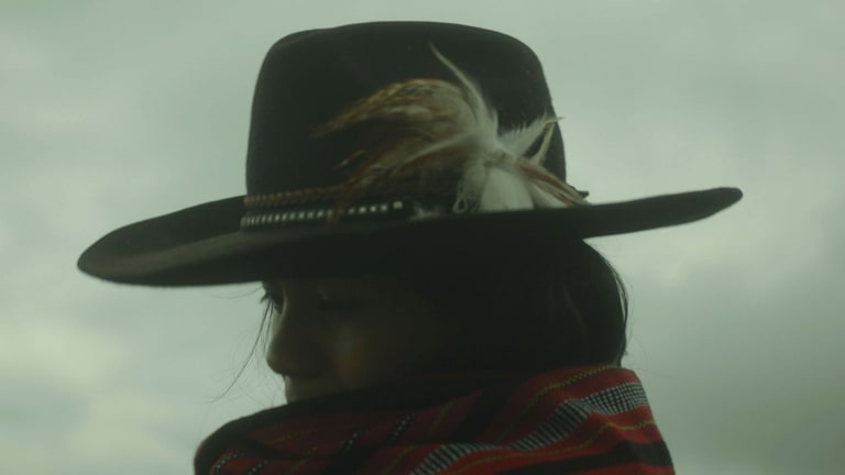 Side profile of a woman in a feathered hat and a red blanket.