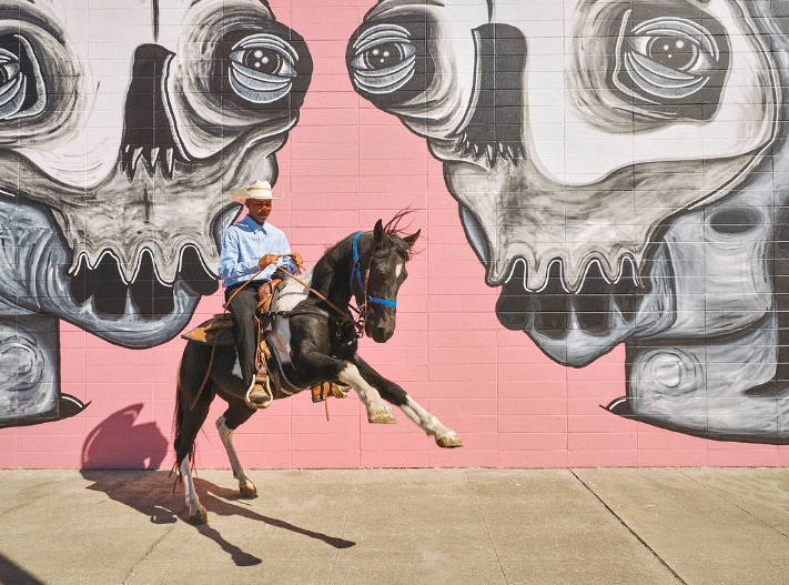 A man riding a horse in front of a mural.