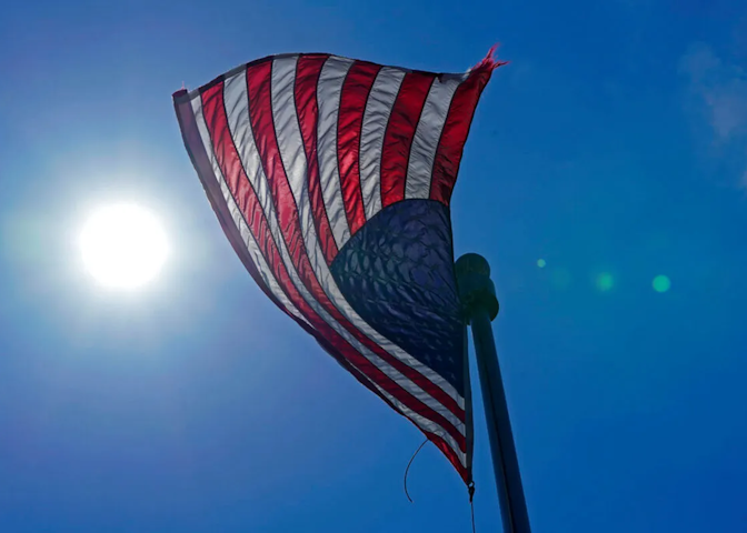 A U.S. flag flying with the sun in the background.