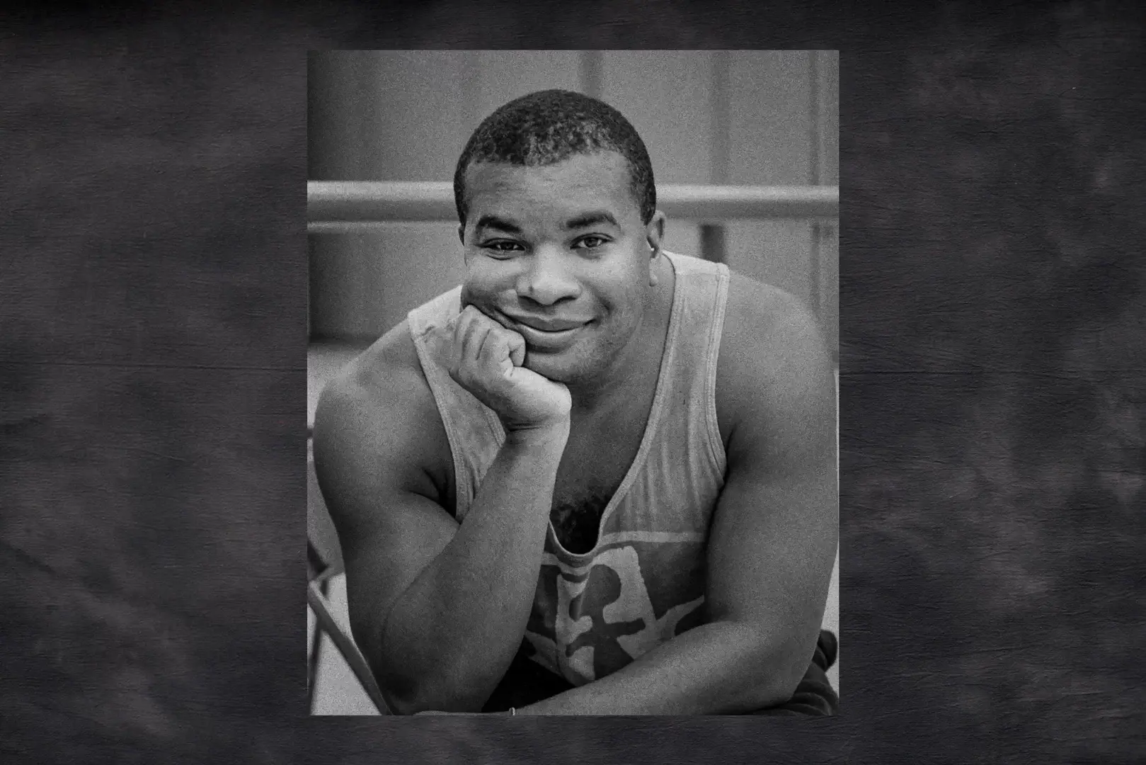 A man in a tank top poses for a picture with his chin in his hand.