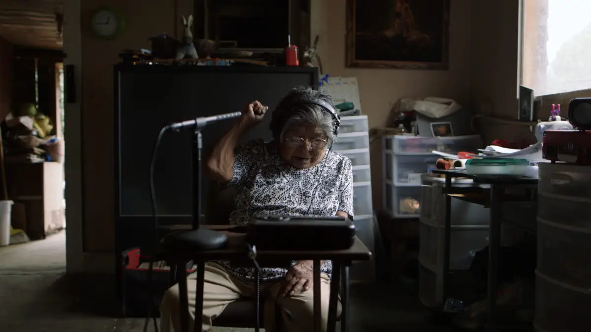 Woman in headphones records on a microphone on a small desk in the center of a study.