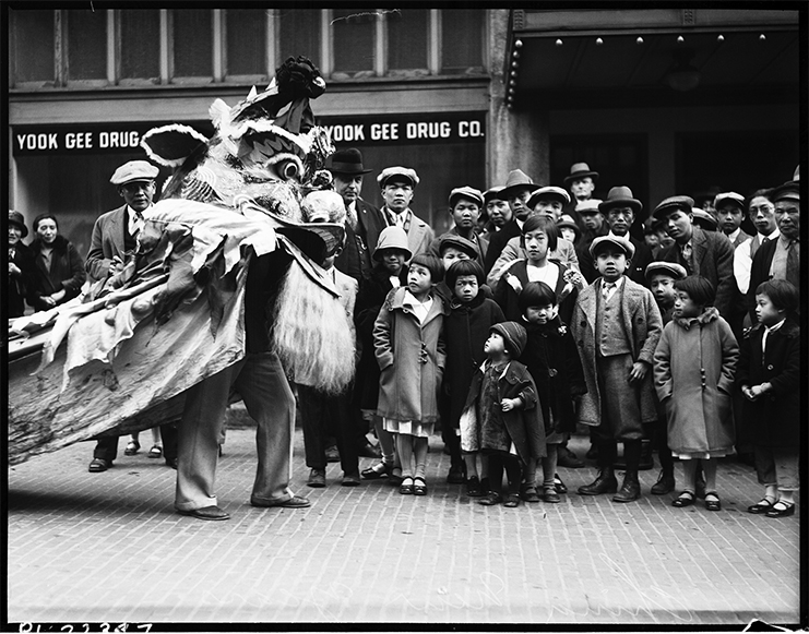 Black and white photo of a dragon dancer on a street performing for a group.