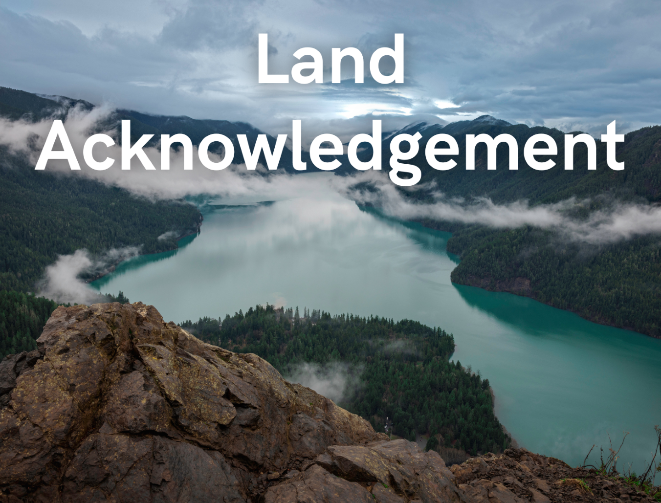 A view from atop a hill overlooking a cloudy lake surrounded by forest and hills with the caption "Land Acknowledgement"