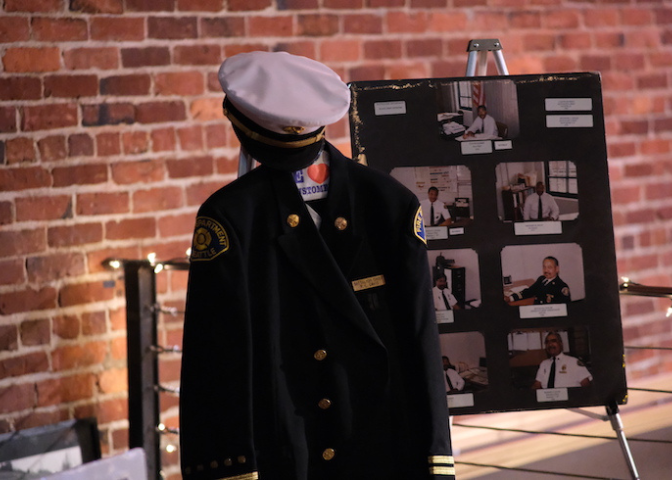 A uniform is displayed in front of a board full of photos of Black firefighters.