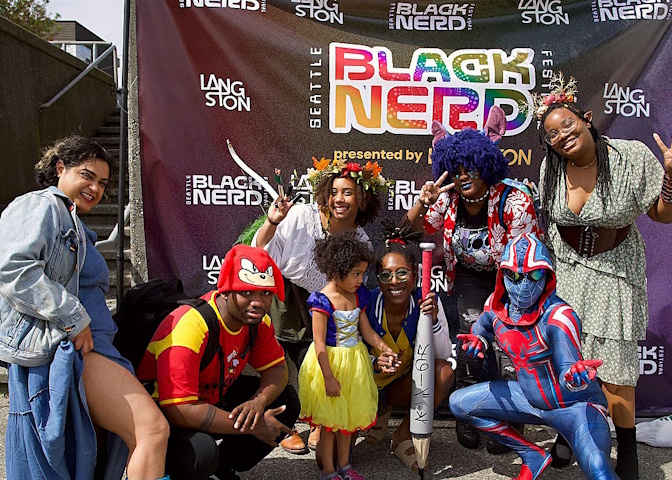 A group of cosplayers pose for a photo in front of a banner for the Seattle Black Nerd Festival.