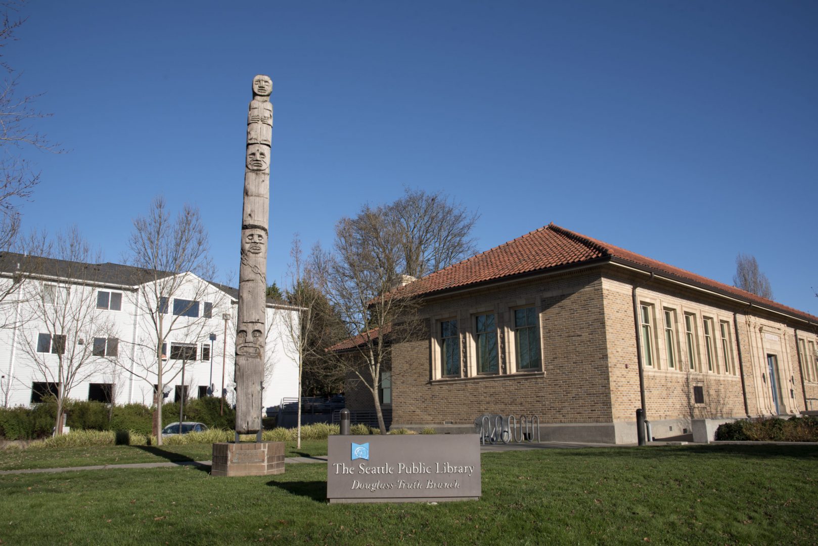 Wood sculpture stands next to a brown, brick library.