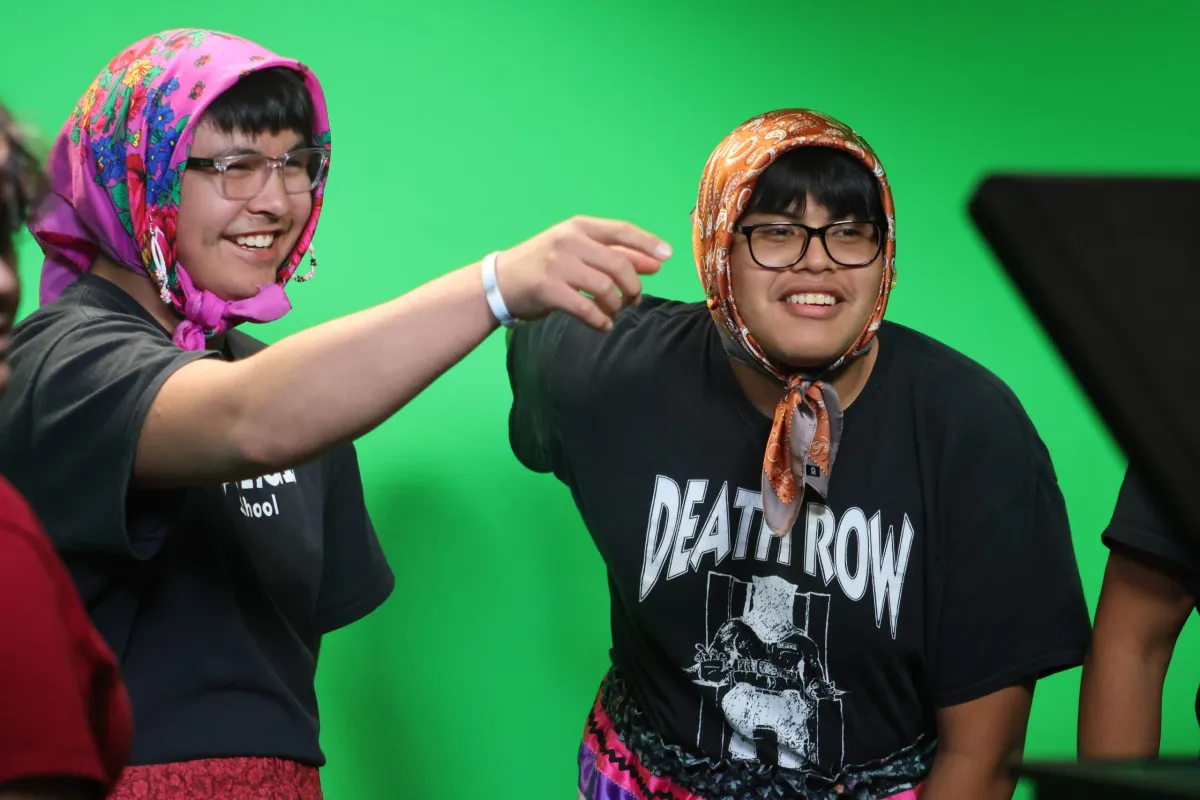 Two students laughing in front of a green screen