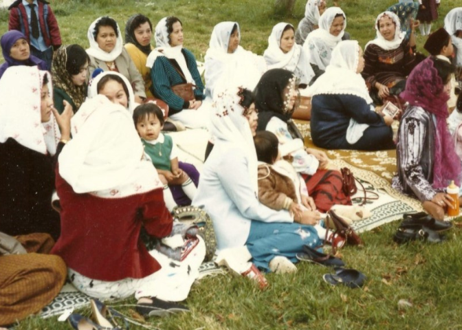 A group of Cham refugees gather on a picnic blanket. Many are wearing headscarves.