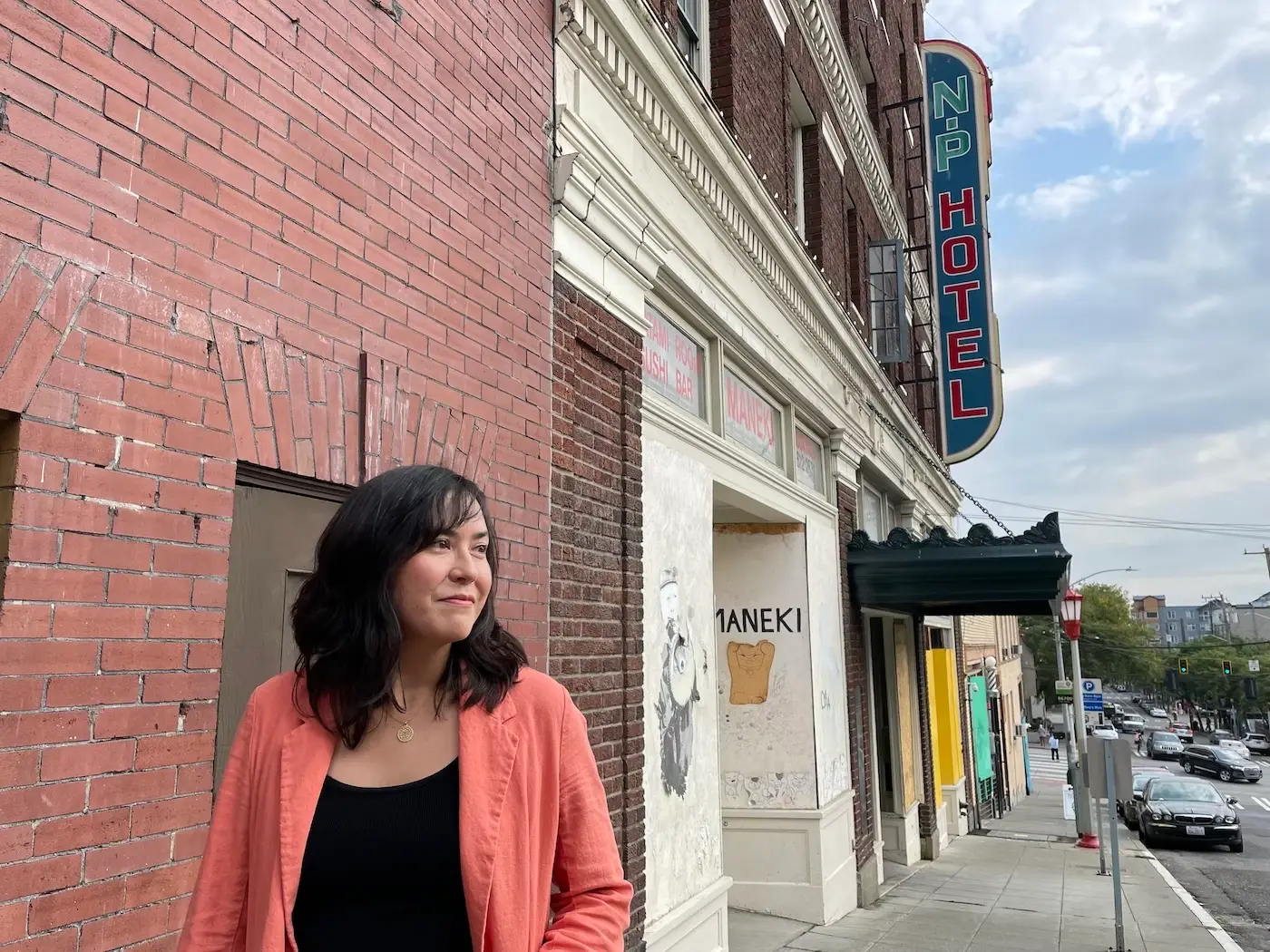 A woman stands on a sidewalk. In the background is a marquee under a sign that says "NP Hotel".