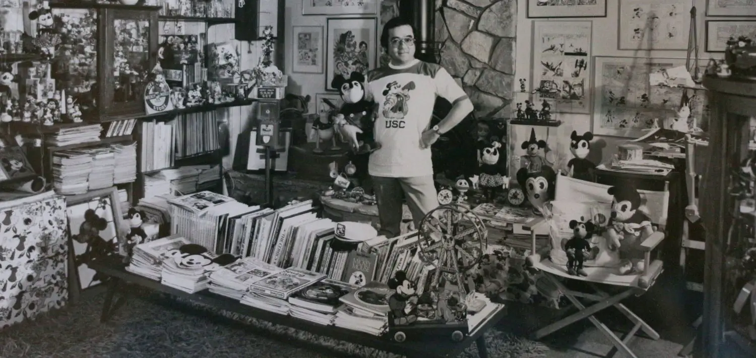 A man stands in the center of a room surrounded by Mickey Mouse collectibles and memorabilia.