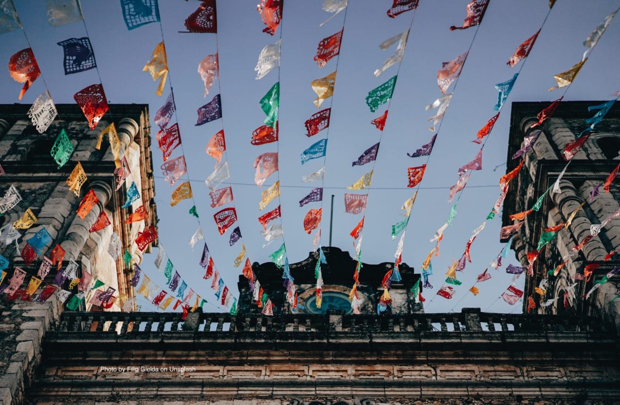 Colorful flags stream above an old building against a blue sky.