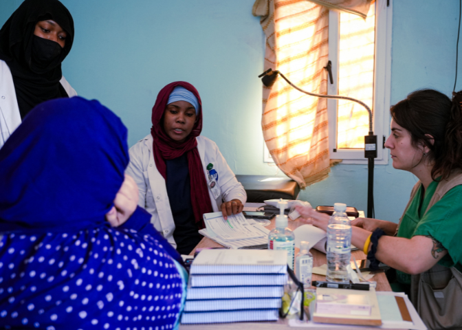 A group of four doctors, all women, sit around a table and discuss patient care. Two of the women are wearing hijabs, one is wearing a niqab.