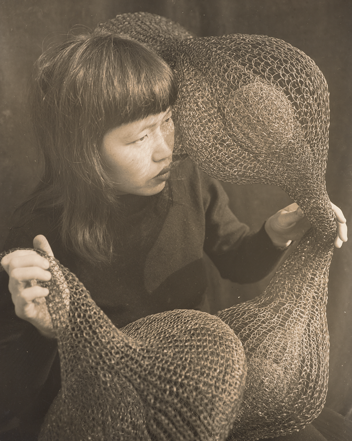 A woman holds one of her sculptures in front of her, she looks off-camera.